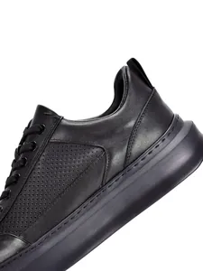 Detalle de cuero negro perforado transpirable en zapatilla de hombre con suela gruesa