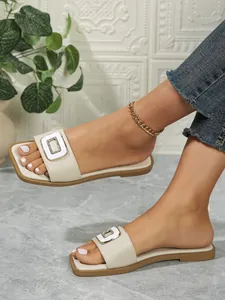 Close-up of stylish off-white square toe flat slides with crystal buckle ornament