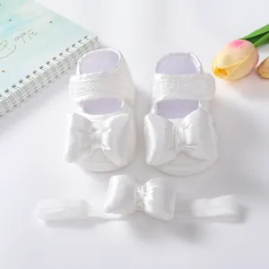 Detailansicht von weißen Baby-Spitzenschuhen mit Satinschleifen und passendem Stirnband.