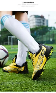 Close-up detail of yellow children's football shoes featuring a black flame design on turf