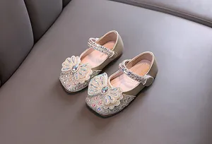 Primer plano de zapatos de princesa dorados para niña con detalle de lazo de strass.