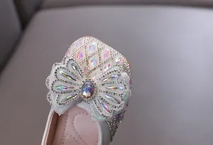 Primer plano del detalle de lazo de pedrería en los zapatos de princesa blancos para niñas