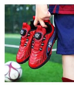 Primo piano di scarpe da calcio rosse per bambini con fibbia rotante tenute su un prato.