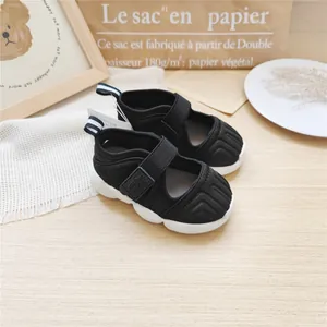 Detailed side view of black children's sports sandals with white soles on wood.