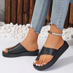 Sandales noires à semelles compensées et anneau d'orteil, portées avec un jean sur gravier