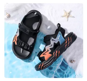Detailaufnahme von schwarzen Jungen-Sandalen mit blau-orangen Akzenten auf Sandhintergrund.