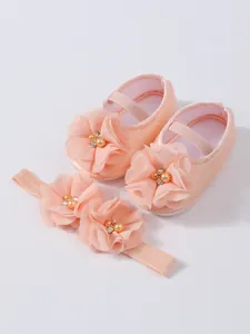 Détail de chaussures de princesse rose pour bébé avec bandeau floral assorti.