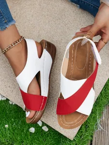 Close-up detail of women's red and white Roman wedge sandals on a stony surface