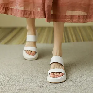 Primer plano de sandalias blancas con suela de plataforma usadas con una falda larga.