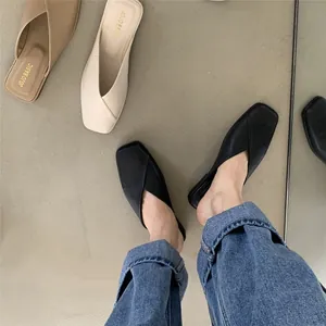 Primo piano di sabot bassi minimalisti a punta quadrata in pelle nera con jeans blu