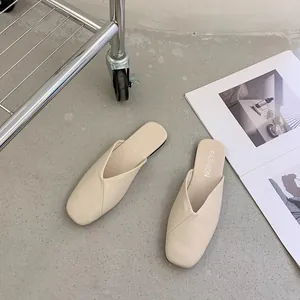 Eleganti sabot bassi color crema su sfondo di cemento dal design minimalista