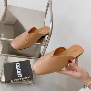 Eleganti sabot beige piatti in morbida pelle mostrati in un primo piano a mano.