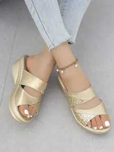 Primo piano di eleganti sandali con zeppa dorati con cinturini glitterati su una modella