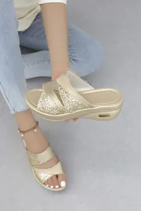 Dettaglio di sandali con zeppa color oro con eleganti cinturini incrociati glitter.