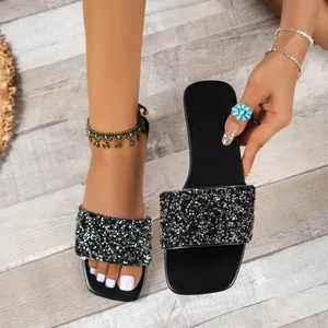 Close-up detail of black sequined slide sandals featuring sparkling rhinestone texture