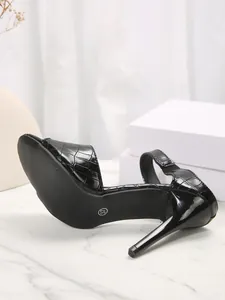 Close-up of black crocodile-embossed high-heel sandals showing stiletto heel and sole detail.