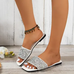 Close-up of sparkling silver sequin flat slides on model's feet in lifestyle setting