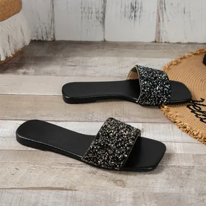 Close-up view of elegant black flat sandals with shimmering sequin strap on wooden floor.