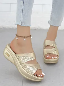 Dettaglio di sandali con zeppa e plateau glitterati oro con cinturini incrociati