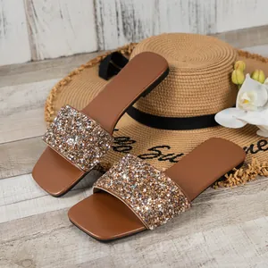 Close-up of brown flat slide sandals with sparkly sequin strap and summer straw hat