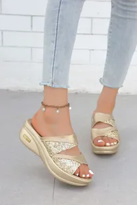 Dettaglio di eleganti sandali con zeppa glitterati color oro e cavigliera di perle
