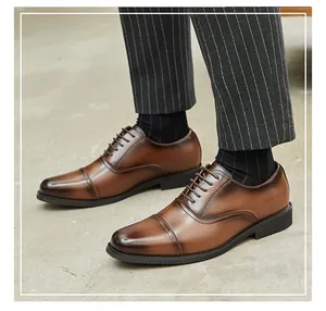 Detail view of brown leather cap-toe Oxford shoes worn with formal striped trousers.