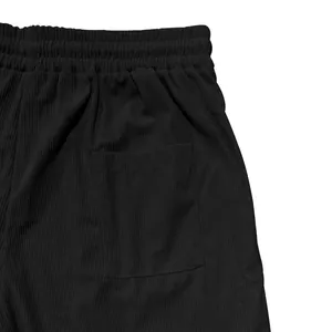Detailopname van de elastische tailleband en zijzak op een zwarte corduroy vrijetijdsshort.