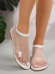 Detalle de sandalias planas de malla blanca con pedrería, punta redonda y diseño calado