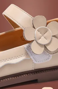 Makroaufnahme von beigen Lederschuhen für Mädchen mit Blumenverzierung und Klettverschluss