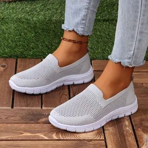 Primo piano di scarpe slip-on in mesh grigio indossate con jeans su una pedana in legno