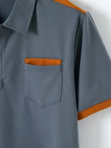 Close-up detail of a grey men's polo shirt featuring an orange trim pocket and sleeve cuff.