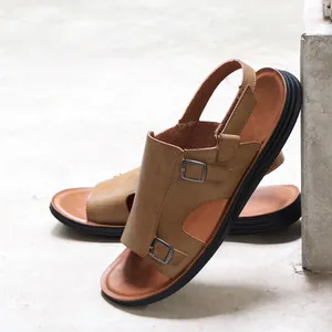 Detailed view of brown leather men's sandals with adjustable buckles on stone floor.
