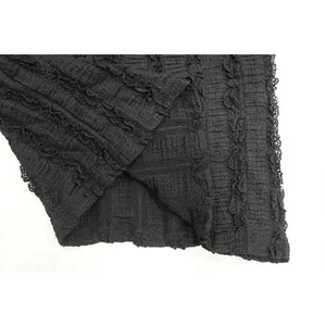 Close-up detail of textured black fabric featuring delicate ruffled lace trim on edges