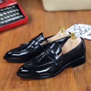 Men's black British style tassel loafers with a vintage pointed toe on a wood floor