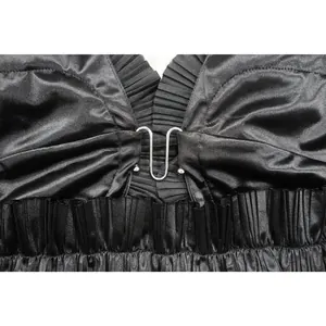 Dettaglio del vestito in raso nero con scollatura a balze pieghettata e fibbia metallica.