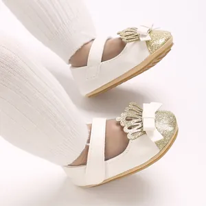 Detailaufnahme weißer Babyschuhe für Mädchen mit goldener Krone, Glitzer und Schleife.