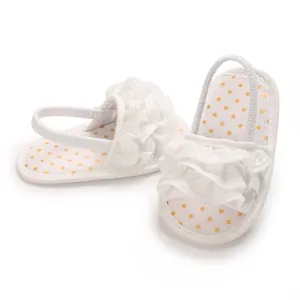 Close-up view of white baby girl sandals featuring yellow polka dots and ruffle straps