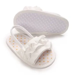 Elegant white ruffled baby girl sandals with polka dot footbed and elastic heel strap.