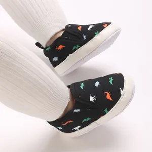 Macro view of baby boy slip-on shoes with colorful dinosaur print on black canvas.