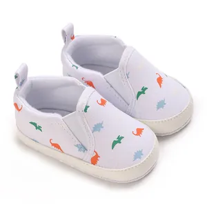 Close-up of soft-sole baby walker shoes with colorful dinosaur print on white canvas.