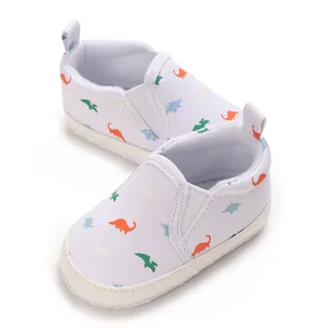 Close-up of white infant walker shoes with colorful dinosaur print and soft soles.