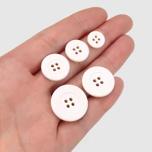Set of five eco-friendly white four-hole cotton buttons displayed on hand for size