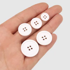 Eco-friendly white four-hole cotton buttons displayed on hand for clothing size scale