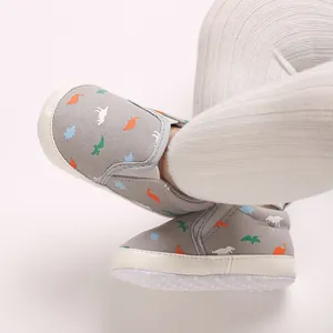 Close-up of gray baby pre-walker shoes with colorful dinosaur prints and soft soles.