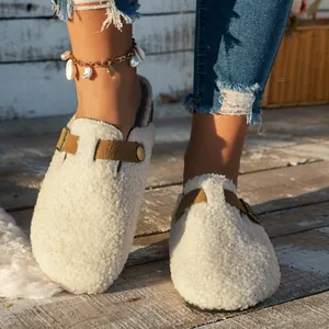 Close-up view of women's cream fuzzy clogs with a brown buckle strap on wooden floor.