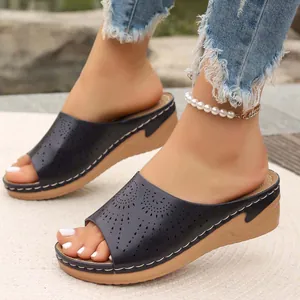 Dettaglio di sandali neri con zeppa in stile retrò con motivi floreali traforati.