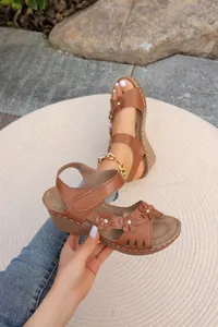 Detailaufnahme brauner Keilsandaletten mit dekorativen Blumen und lasergeschnittenem Design