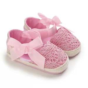 Detailed view of pink lace baby sandals featuring a decorative ribbon bow and soft woven sole