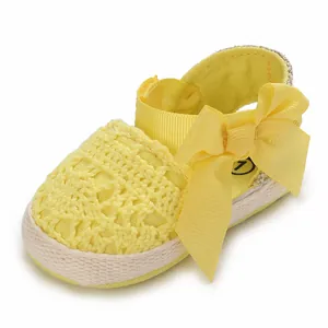Close-up of yellow newborn baby girl lace sandals with a large decorative ribbon bow.