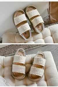 Detailed view of girls' white lace sandals with soft brown soles and pom-pom trim